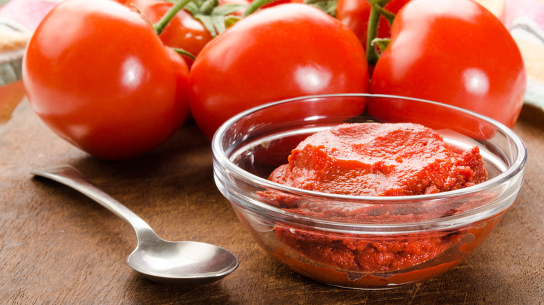 A small, clear, glass bowl in front of tomatoes on the vine.