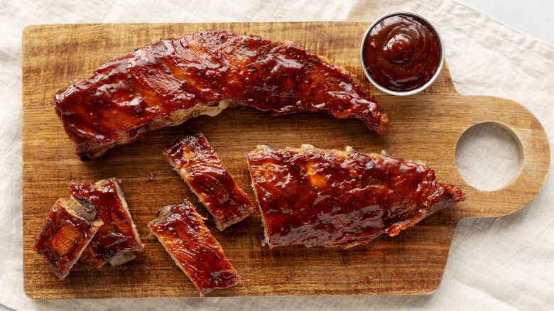 Baby back ribs with side of sauce on a wood platter