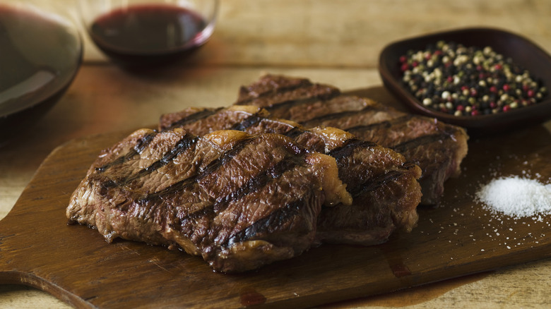 steaks on cutting board with bowl of peppercorns and salt