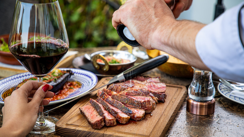 glass of red wine and hands salting board of steak