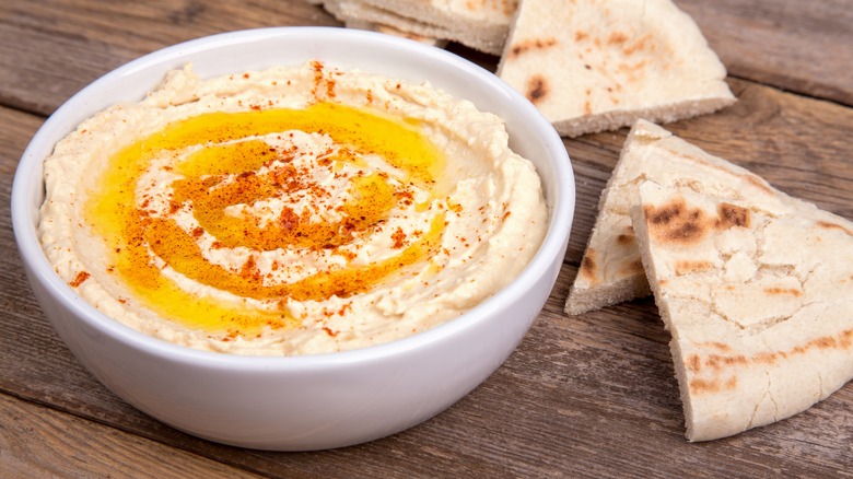 A bowl of warm hummus, topped with olive oil and paprika, surrounded by slices of pita bread