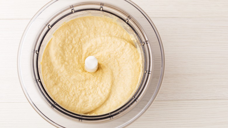 A food processor full of creamy hummus on a white wooden table