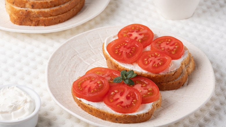 Two thick slices of toast with cream cheese and sliced tomatoes sit on a plate.