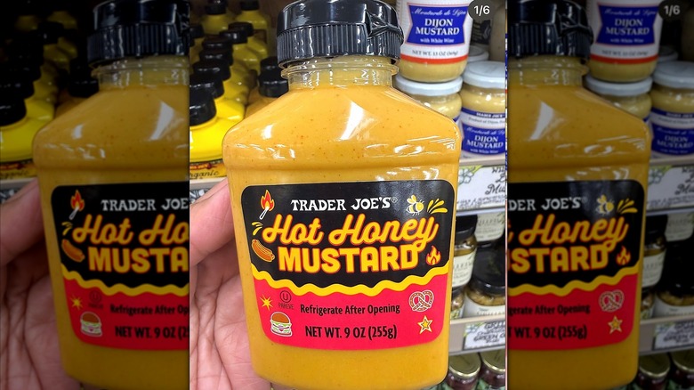 A hand is holding a bottle of Trader Joe's Hot Honey mustard in store.