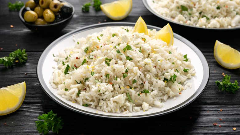 A bowl of rice with lemon and parsley, with a bowl of olives in the background