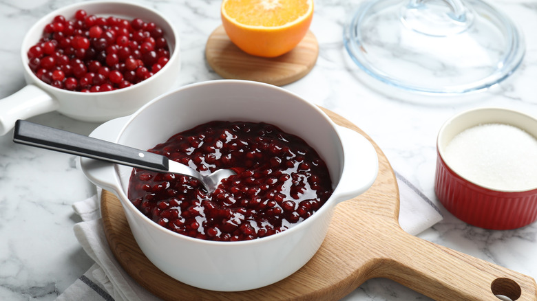 Fresh cranberry sauce is displayed in bowl next to fresh cranberries, an orange half, and a bowl of sugar.