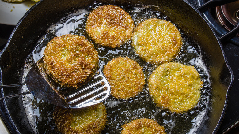 Slices of green tomato being fried in a frying pan