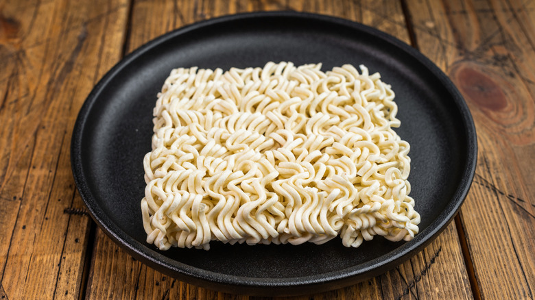 A block of dry instant ramen on a black plate on a wooden surface