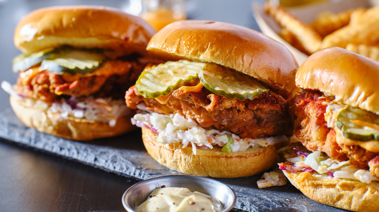 Row of three Nashville hot chicken sandwiches with pickles and slaw