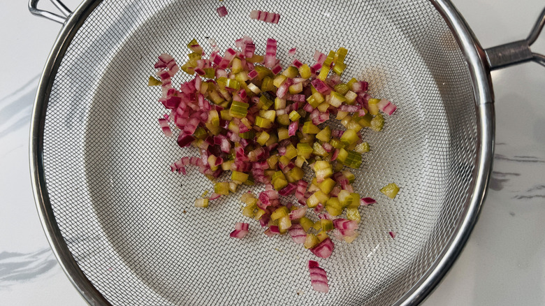 pickled celery and onion straining in a colander over a dish