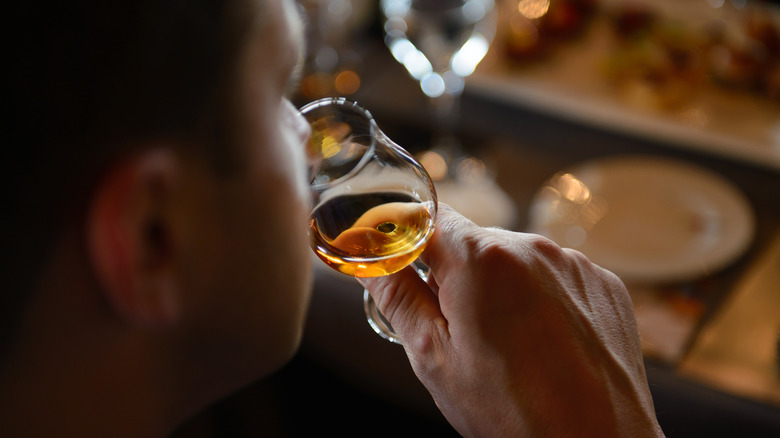 An over the shoulder shot of a person smelling a glass of whiskey