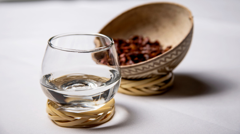 Tequila in a tasting glass next to dried red chili in a bowl