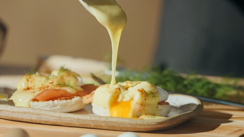 Hollandaise sauce made by tempering eggs poured onto poached eggs