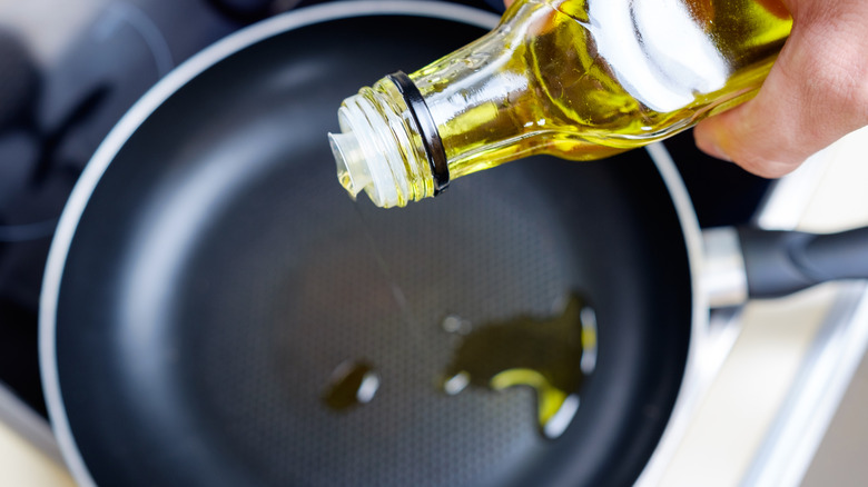 A hand pours olive oil into a frying pan.
