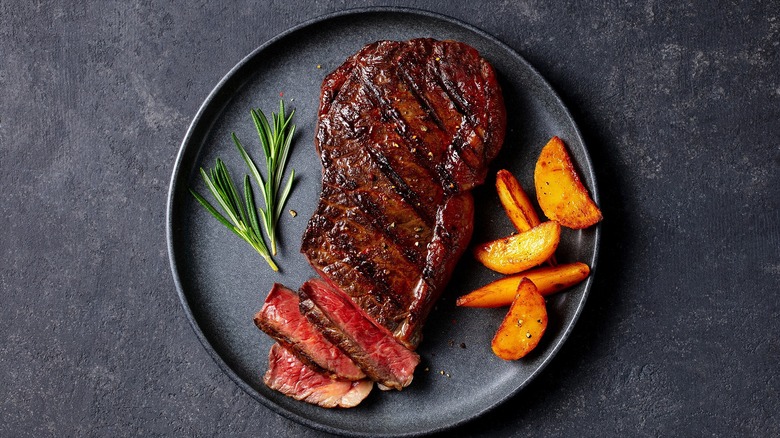 juicy prime rib on a black plate with rosemary and a few potato wedges