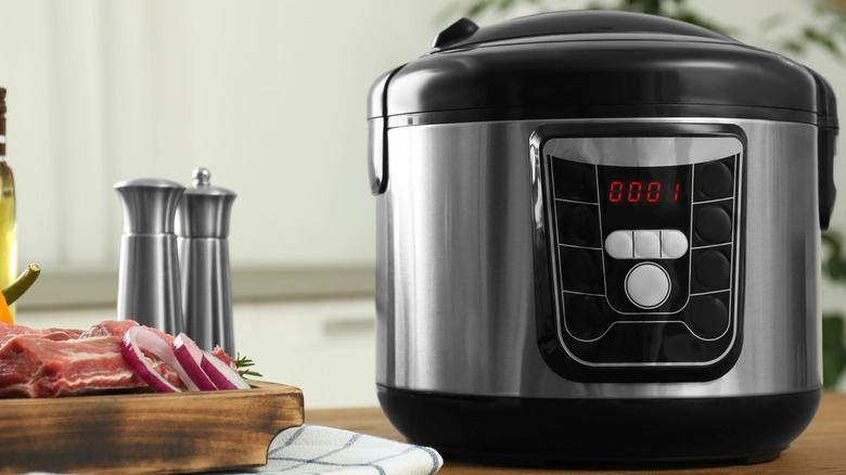 slow cooker next to a wooden board with raw prime ribs and sliced red onions