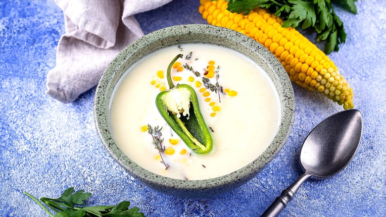 Bowl of cream corn soup topped with sprigs of thyme and half of a raw jalapeño