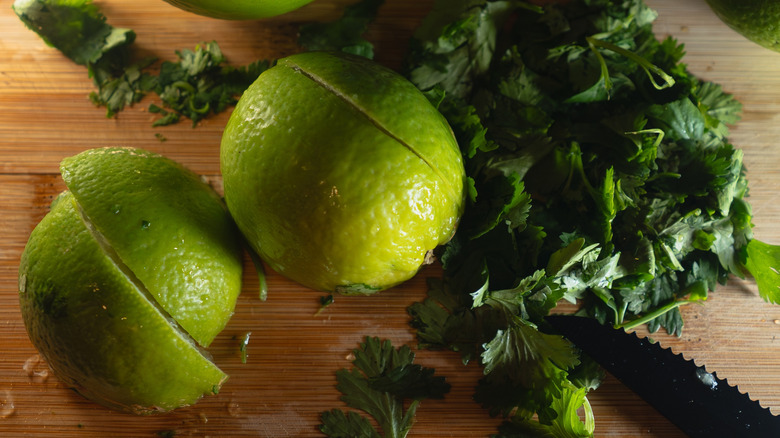 Limes and cilantro on a cutting board are photographed from above.