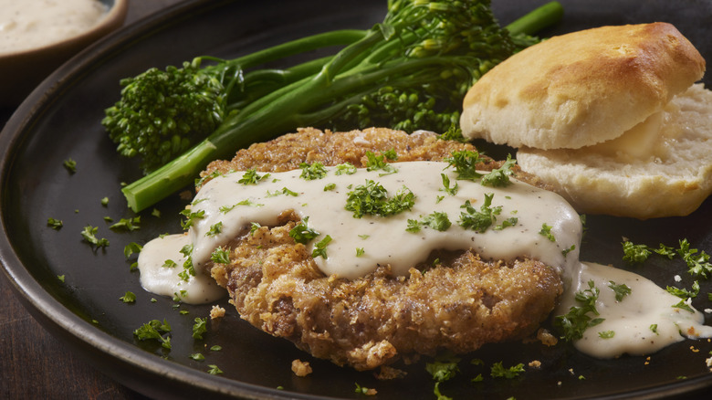 A plate of chicken fried steak served with broccolini and a biscuit with butter