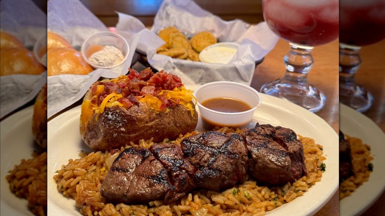 Texas Roadhouse steak medallions on top of rice with a loaded baked potato