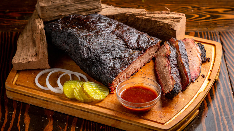 Brisket on a wooden board with pickles and onions
