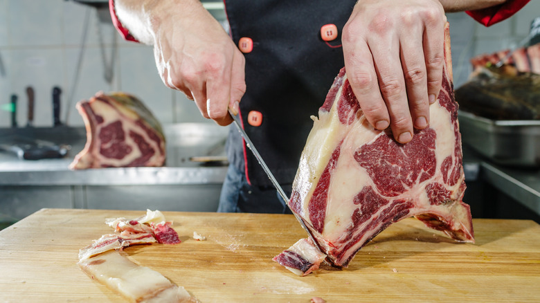 Chef trimming a steak on a cutting board
