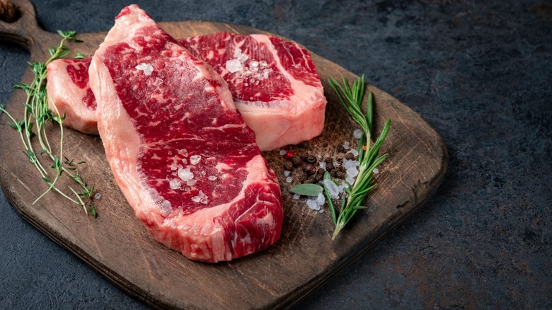 raw new york strip steaks and herbs on a wooden board