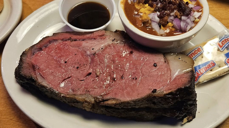 Texas Roadhouse prime rib served alongside chili, with an au jus sauce and crackers on plate.