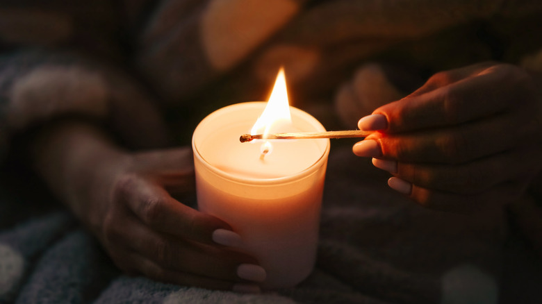 A person's hand is seen lighting a candle with a match.