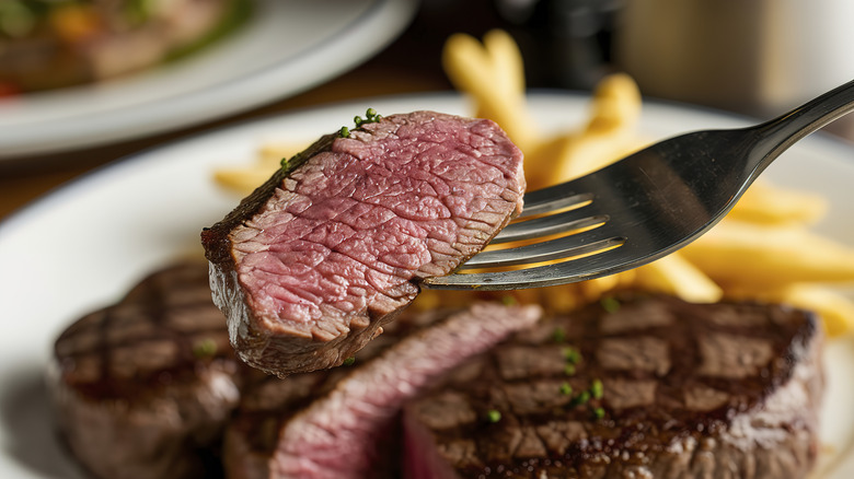 Fork with a bite of steak in front of steak and fries in the background