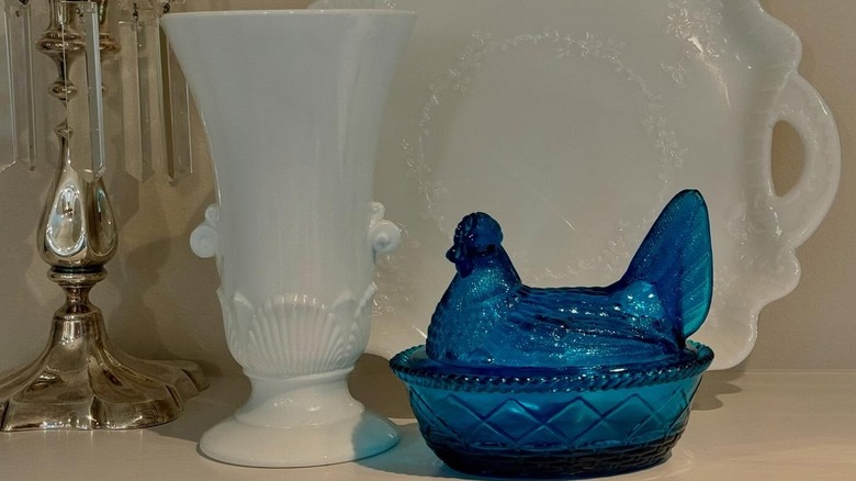 A cobalt blue hen on a nest next to pieces of milk glass.