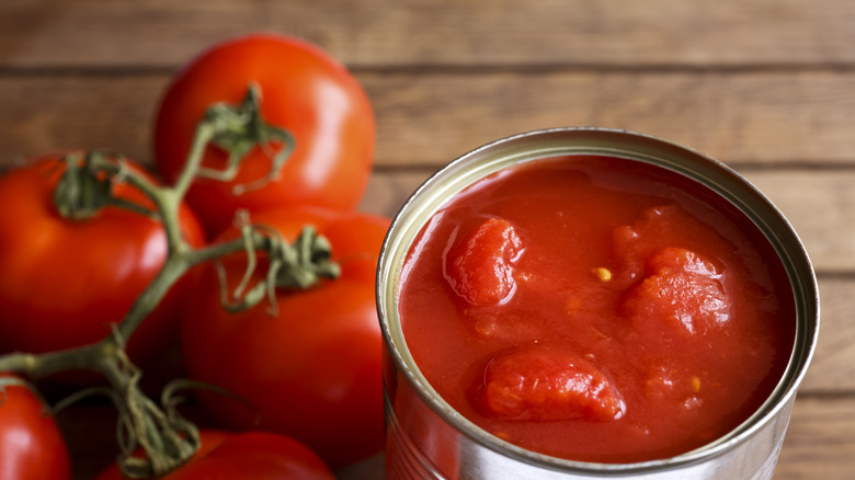 chopped tomatoes in a metal tin with fresh tomatoes on the wooden table