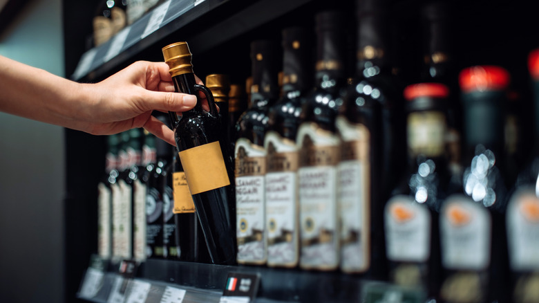Someone taking a bottle from a row of balsamic vinegar products at the grocery store