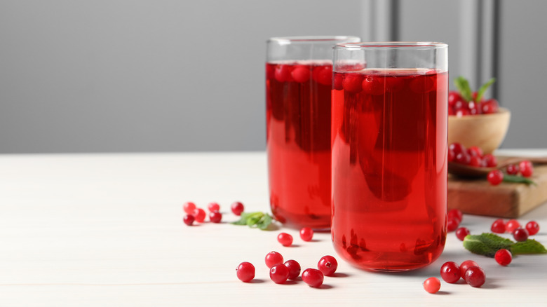 Cranberry juice in two glasses with fresh cranberries scattered around them