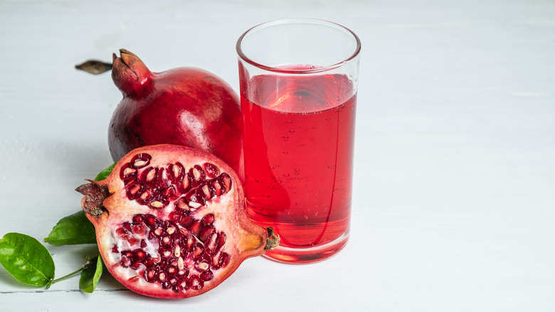 A glass of pomegranate juice and whole pomegranates on a light background