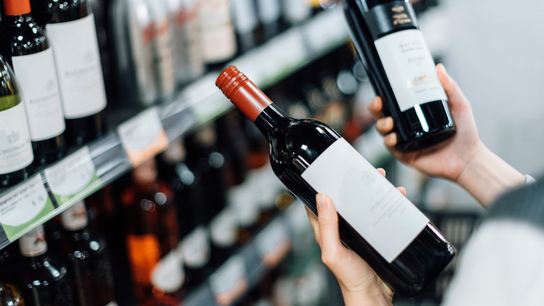 A person in a grocery store holding up and comparing two bottles of red wine in their hands