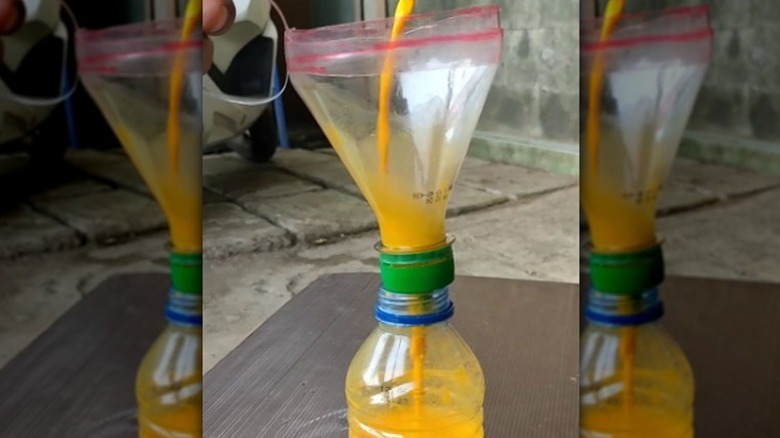 Pouring orange liquid into a funnel made out of a plastic bottle
