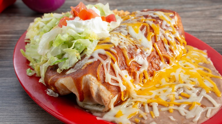 Smothered burrito with red chile, garnishes, and melted cheese