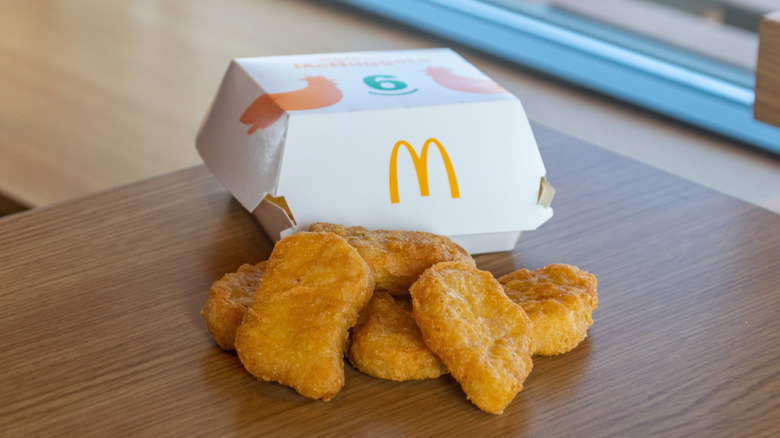 A McDonalds chicken McNuggets container with six nuggets in front of it.