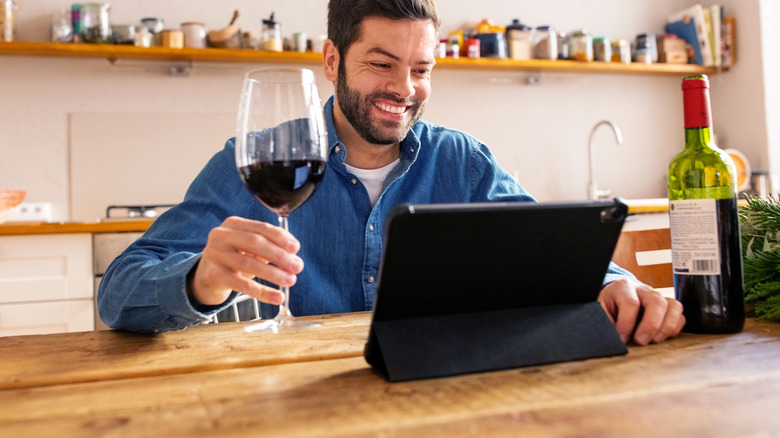 Man holding glass of wine in front of computer