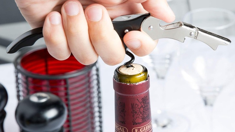 person pulling wine cork out with corkscrew