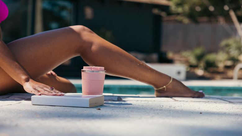 Woman sitting by pool with wine tumbler