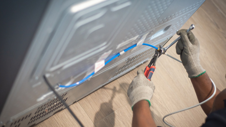 Person installing a water line behind a fridge