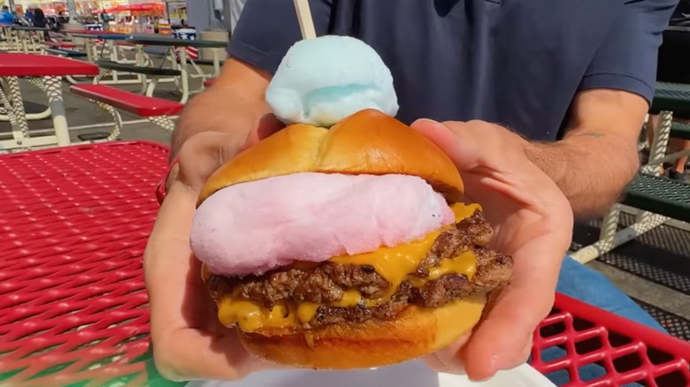 hand holding a cheeseburger with pink and blue cotton candy on it