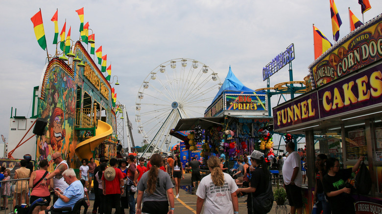 People at fair with variety of rides, games, and food booths