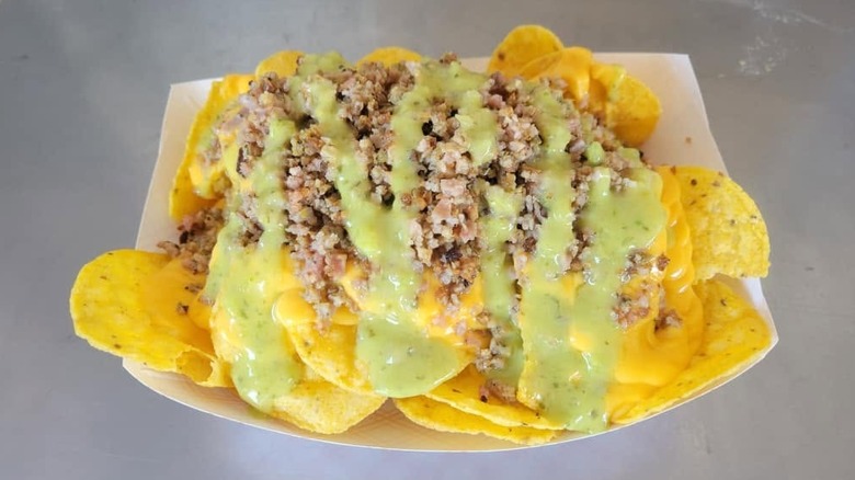 A tray of nachos topped with rattlesnake bits and avocado and green chili salsa
