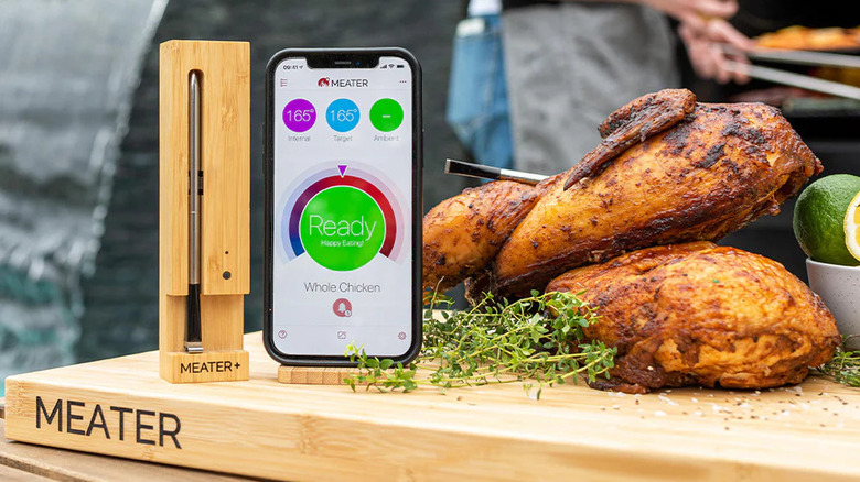 A Meater Plus Smart Bluetooth Wireless Meat Thermometer on a cutting board next to a smart phone and a roast chicken