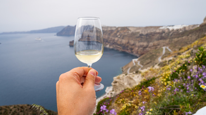 Hand holding glass of Assyrtiko wine overlooking cliffs in Greece