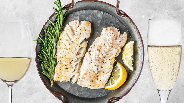 Plate of flaky white fish flanked by glasses of white wine