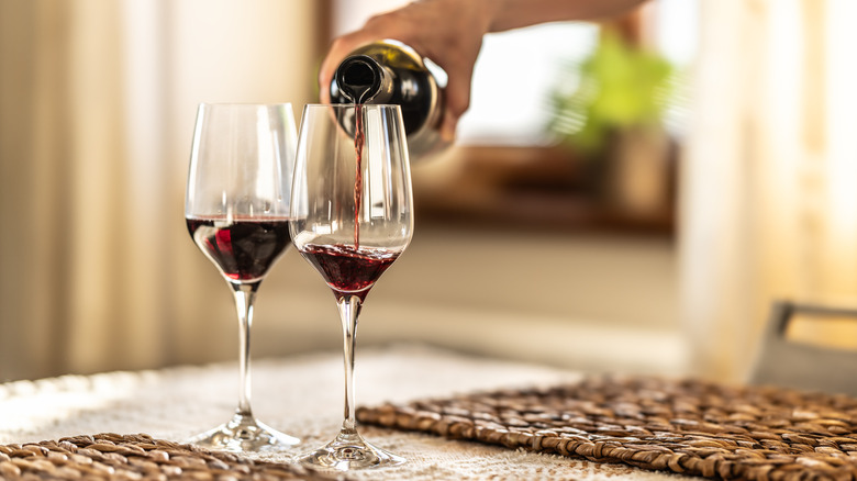 Hand pouring red wine into two wine glasses